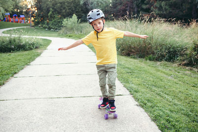 Happy caucasian boy in grey helmet riding skateboard on road in parkboy learning to ride skateboard.