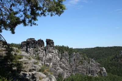 Low angle view of rock formation amidst trees against sky