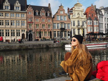 Woman with umbrella in canal against buildings in city