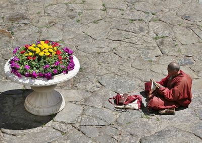 High angle view of monk reading religious book by flower vase