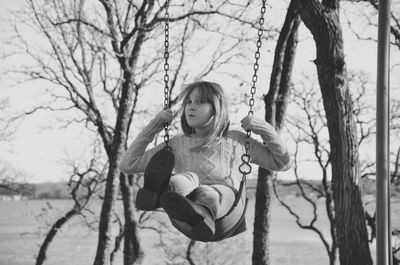 Portrait of girl swinging against bare trees at park