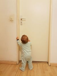 Rear view of baby girl standing by closed door at home
