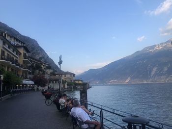 People sitting on mountain by lake against sky