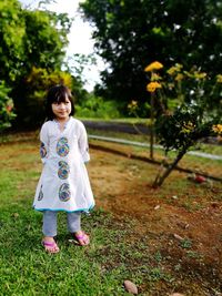 Full length of smiling girl standing on field at park