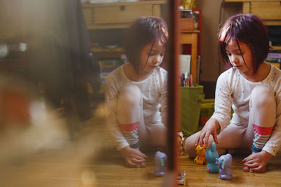 A small child sits reflected in glass playing with toys on wood floor