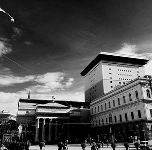 People walking on city street against cloudy sky