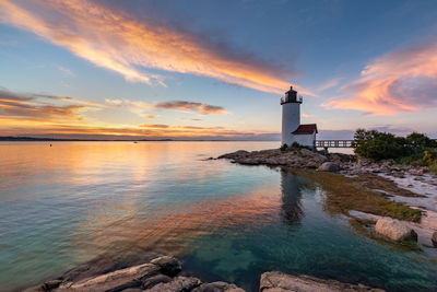 Lighthouse by sea against sky during sunset