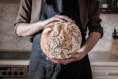 Midsection of baker holding baked bread in bakery