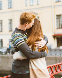 Couple embracing while standing against building