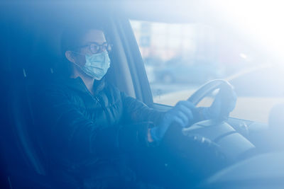 Pretty caucasian woman with glasses, anti virus medical mask and blue latex gloves driving a car