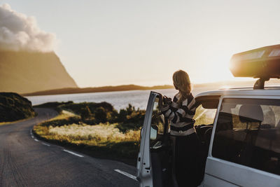 Woman standing by car on road during sunset