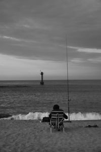 Rear view of man sitting at beach against sky