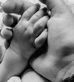 Close-up of parent and baby holding hands on bed