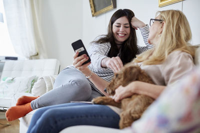 Mother showing mobile phone while daughter playing with dog on sofa at home