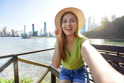 Portrait of young woman wearing hat standing against river