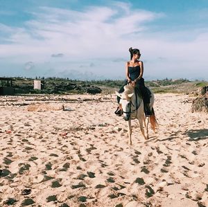 Woman riding horse on sand against sky