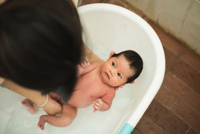 High angle view of mother holding naked newborn daughter in bathtub