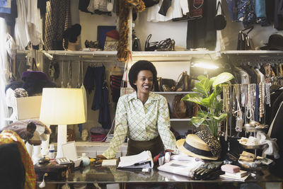 Smiling female owner looking away while standing at counter in clothing store