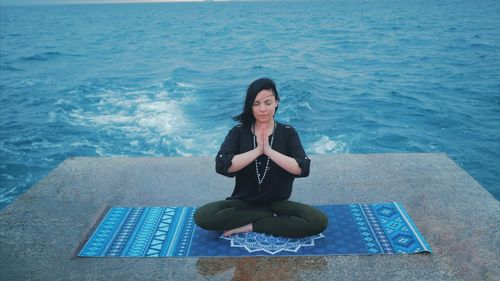 Full length of woman performing yoga against sea