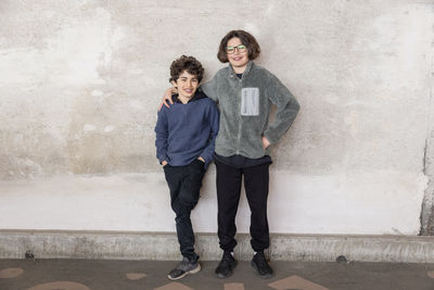 Portrait of smiling brothers standing against wall at recycling center
