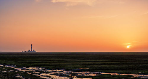 Lighthouse by sea against sky during sunset