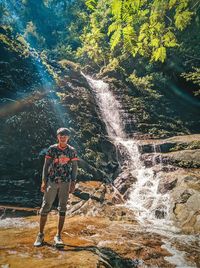 Full length of man standing by waterfall in forest