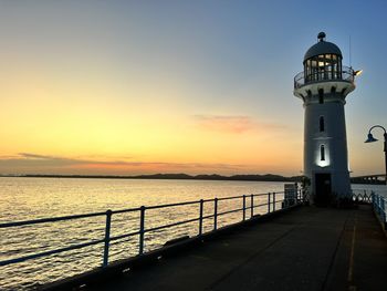 Lighthouse by sea against sky during sunset