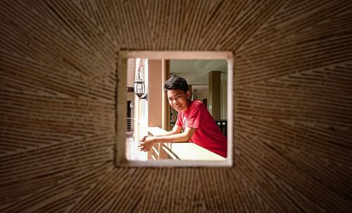 Portrait of smiling boy seen through hole leaning on railing at home