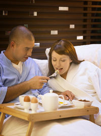 Smiling mid adult man feeding girlfriend on bed at home