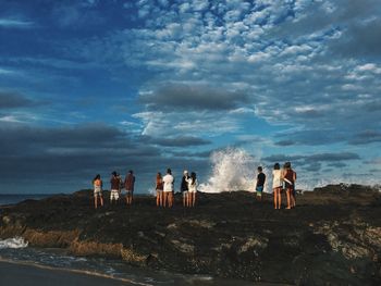 People on beach against cloudy sky