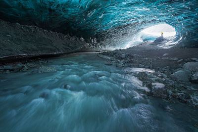 Tourist in outerwear standing near uneven holes in ice surface while exploring cave in vatnajokull glacier on winter day in iceland