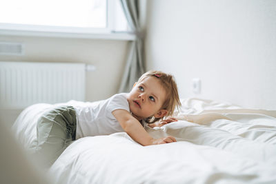 Cute funny baby girl in home clothes lies on bed at home