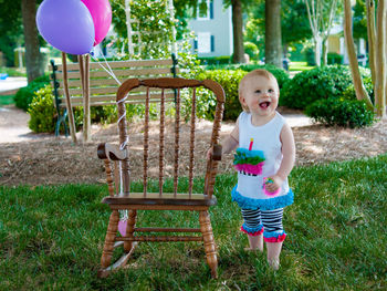 Innocent girl standing by rocking chair with balloons at park