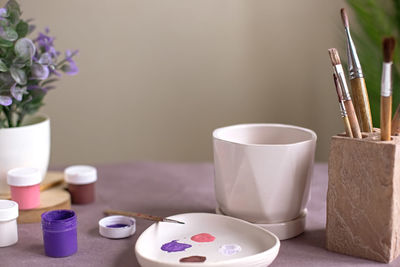 A still life with a white ceramic flower pot stands on a table with crafting tools