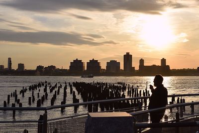 Silhouette man standing by hudson river against sky during sunset