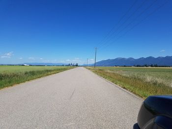 Road amidst field against clear blue sky