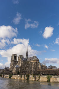 Buildings by river against cloudy sky