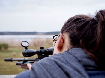 Close-up of woman aiming with rifle against sky