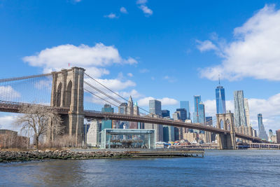 Bridge over river by buildings against sky