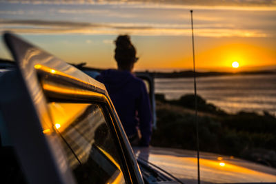 Man standing on car against sky during sunset