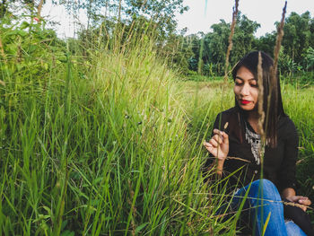 Beautiful young woman sitting on field against trees