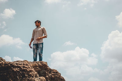 Low angle view of man standing on rock against sky
