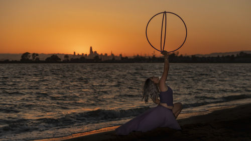 Woman holding hula hoops at beach against sky during sunset