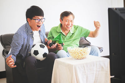 Cheerful father and son cheering while watching tv set at home