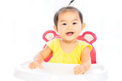 Portrait of cute baby girl sitting on high chair against white background