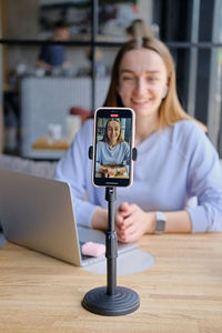 Young beautiful woman blogger making a video for her blog using phone camera in a cafe.