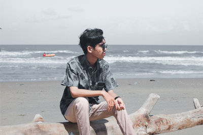 Young man sitting on shore at beach against sky