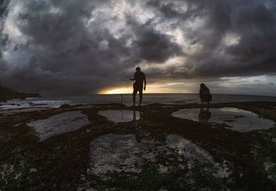 Silhouette man standing on beach against sky during sunset