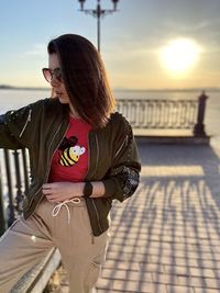 Midsection of woman standing by railing against sky during sunset