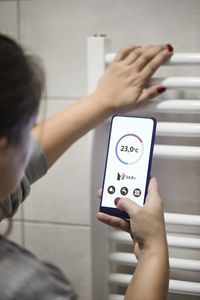 Woman adjusting temperature through mobile by heating boiler